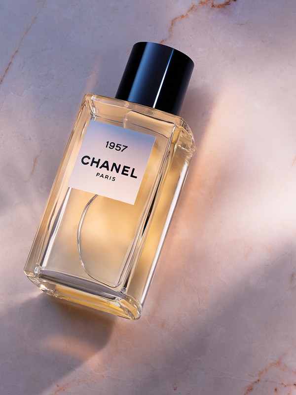 A rectangular glass bottle of Chanel 1957 perfume resting on a polished pink marble surface with soft light.
