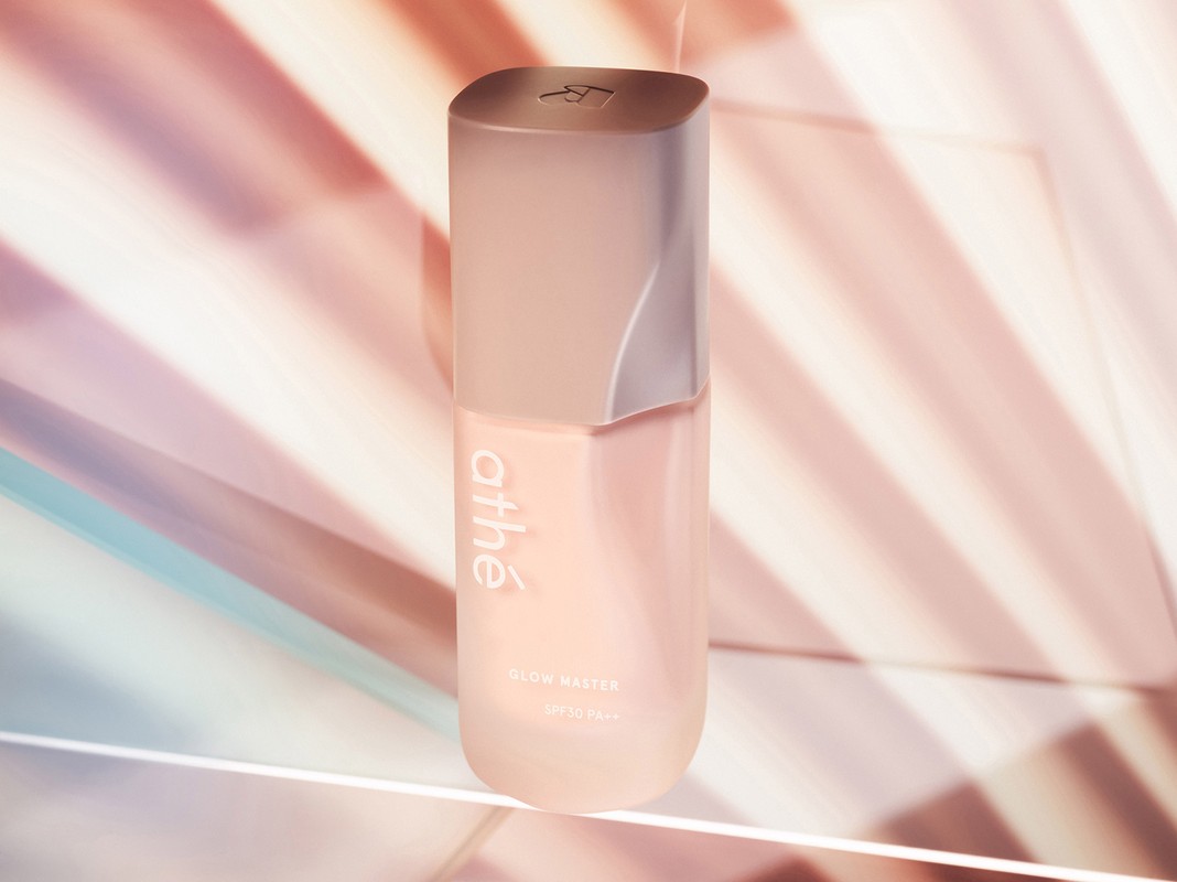 Athe Glow Master SPF 50+ PA++++ cosmetic product bottle in a studio setup with pink and blue background lighting.