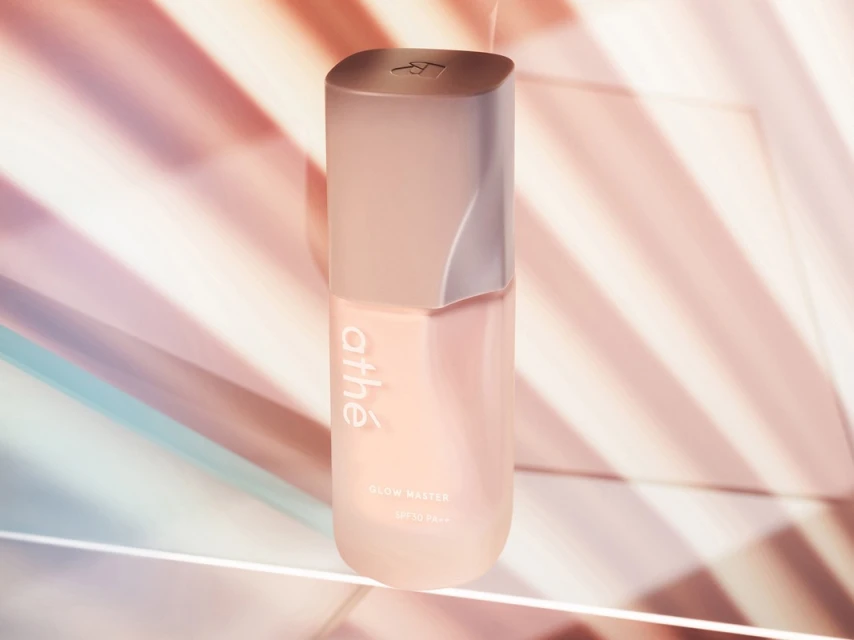 Athe Glow Master SPF 50+ PA++++ cosmetic product bottle in a studio setup with pink and blue background lighting.