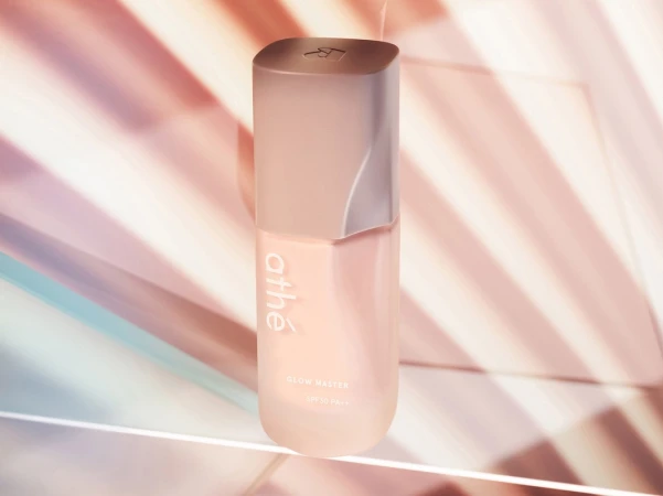 Athe Glow Master SPF 50+ PA++++ cosmetic product bottle in a studio setup with pink and blue background lighting.