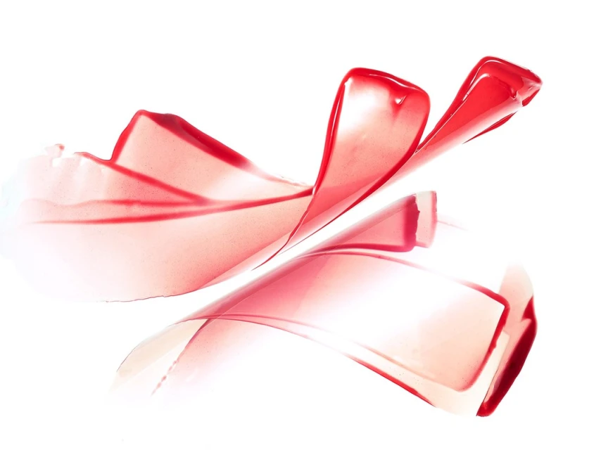 Abstract still life of transparent red ribbons cascading on a seamless white backdrop, creating flowing curves and soft, glossy reflections.