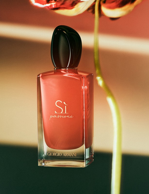 Giorgio Armani Si Passione perfume bottle against a blurred background of a flower and stripes in muted coral and beige tones.