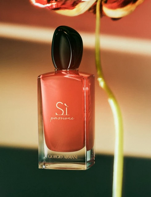Giorgio Armani Si Passione perfume bottle against a blurred background of a flower and stripes in muted coral and beige tones.