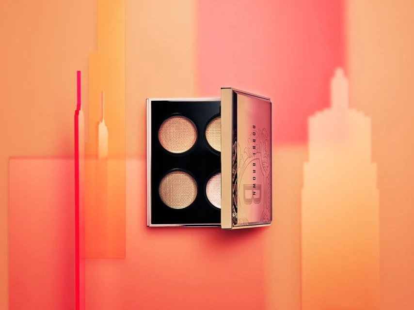 Bobbi Brown eyeshadow palette featuring four shades of shimmering golden and bronze tones, presented on a peach-colored backdrop with geometric shapes.
