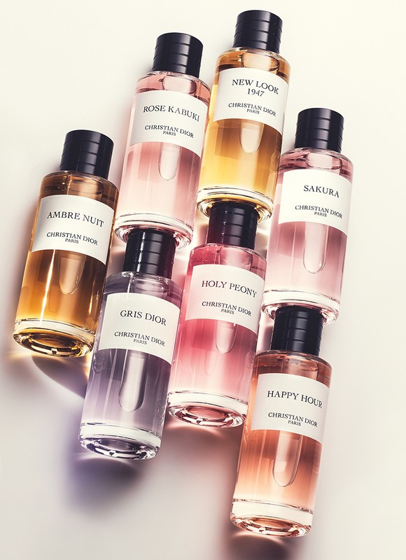 Seven clear glass Christian Dior perfume bottles with black caps, filled with various colored liquids, arranged against a white background.