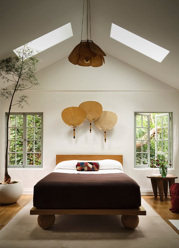 Cozy bedroom interior with a wooden bed, natural light from skylights, and decorative fan art adding a touch of elegance and tranquility.