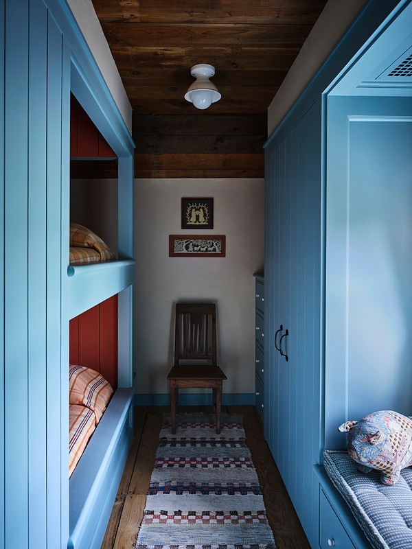 Cozy bunk beds in a narrow hallway feature pastel blue wood, a patterned rug, and soft lighting for a warm, inviting atmosphere.
