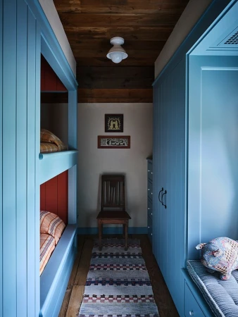 Cozy bunk beds in a narrow hallway feature pastel blue wood, a patterned rug, and soft lighting for a warm, inviting atmosphere.