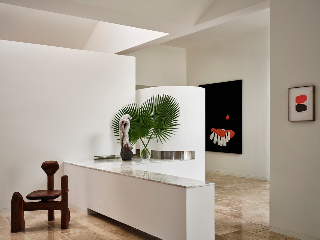 Modern interior with a wooden chair, palm fronds in a vase on a marble-topped partition, and abstract artwork on the walls.