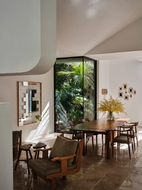 Sunlit dining area showcases wooden table set for six, surrounded by chairs and complemented by a lush garden view through a window.