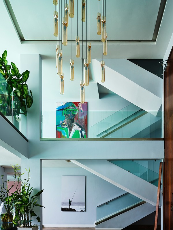 Contemporary home interior featuring a modern staircase, a stylish chandelier, abstract art, and lush potted plants for a vibrant atmosphere.