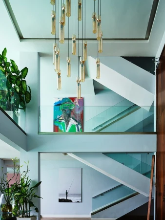 Contemporary home interior featuring a modern staircase, a stylish chandelier, abstract art, and lush potted plants for a vibrant atmosphere.