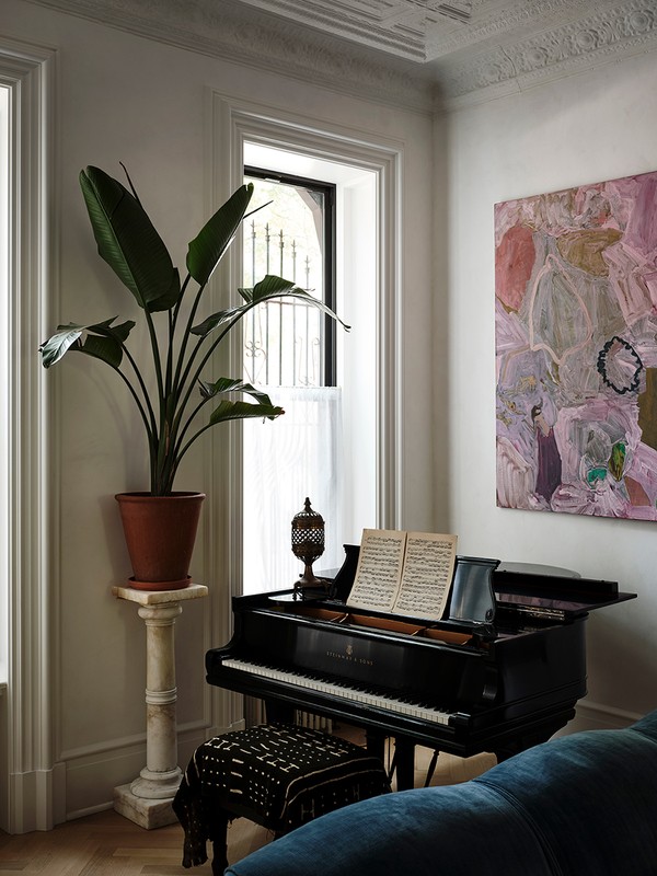 Interior corner featuring a black grand piano with sheet music, a potted plant on a pedestal, abstract art, and a patterned stool.