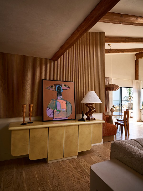 Interior living space showcases an abstract art piece atop a tan cabinet, complemented by wood accents, a lamp, and natural light.