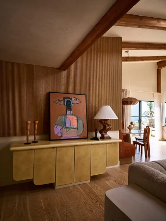 Interior living space showcases an abstract art piece atop a tan cabinet, complemented by wood accents, a lamp, and natural light.