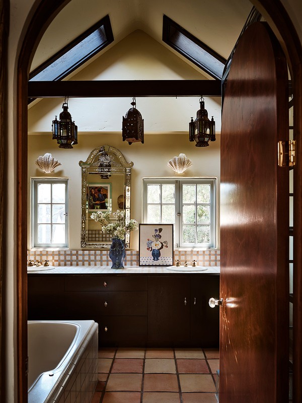 Bathroom interior featuring dark vanity with white countertop, decorative mirror, sconces, and hanging lanterns, plus terra cotta tile.