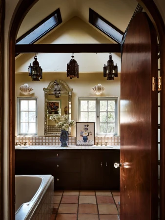 Bathroom interior featuring dark vanity with white countertop, decorative mirror, sconces, and hanging lanterns, plus terra cotta tile.