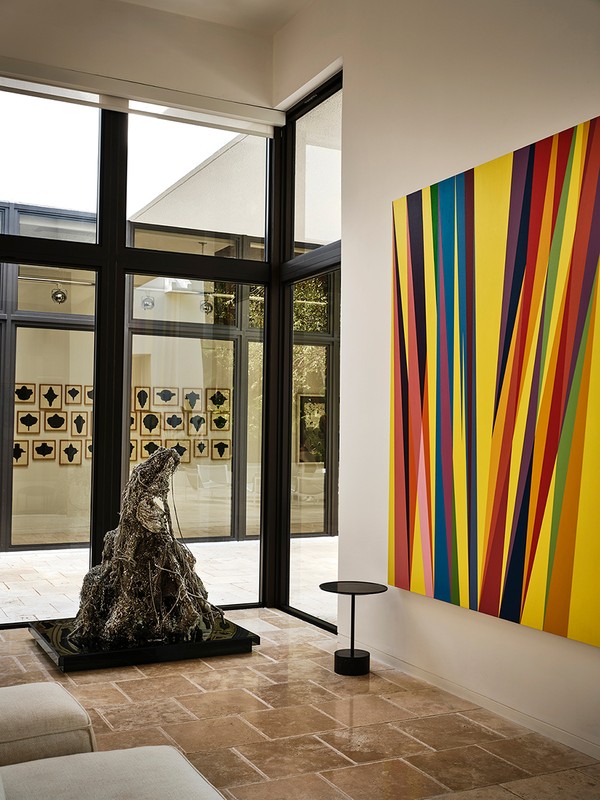 Modern living room interior with a large abstract painting, a metal sculpture, and natural light from a large window.