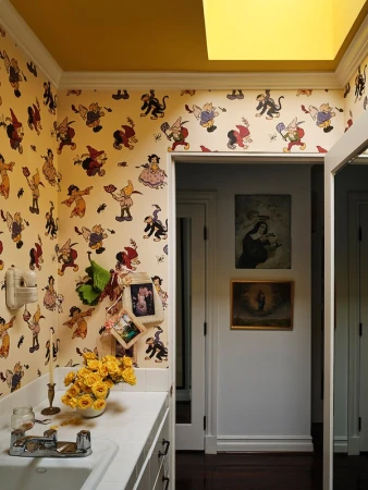 Whimsical bathroom interior featuring cartoon character wallpaper, a white countertop with yellow flowers, and artwork in a hallway.
