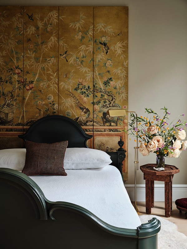 Interior view of a bedroom with a dark wood bed, white linens, floral display, and scenic wallpaper creating an intimate ambiance.