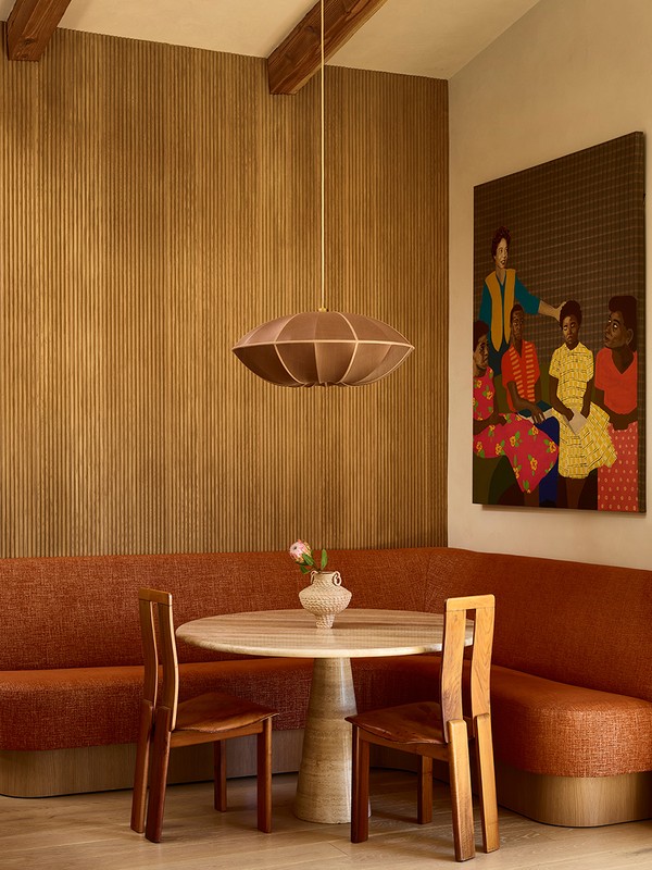 Dining room interior featuring a round marble table, wooden chairs, burnt-orange upholstered bench against a wood-paneled wall. 