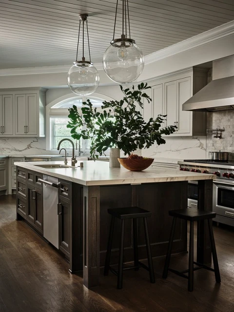 Kitchen interior featuring a marble countertop island with dark wood cabinetry, two black stools, and glass pendant lights.