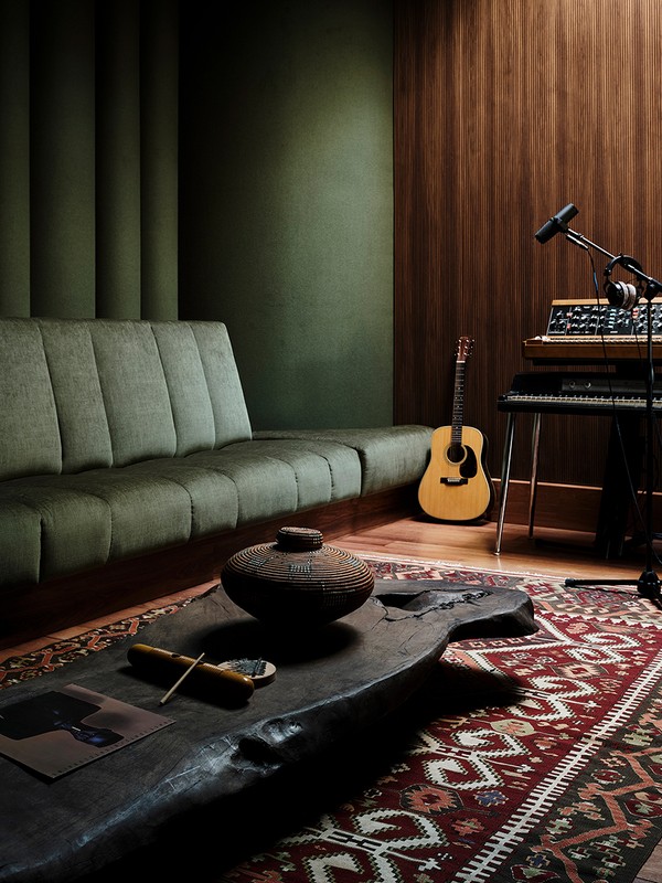 Interior of a music studio with a gray sofa, wooden coffee table, tribal rug, guitar, keyboard, and a microphone, creating a cozy space.