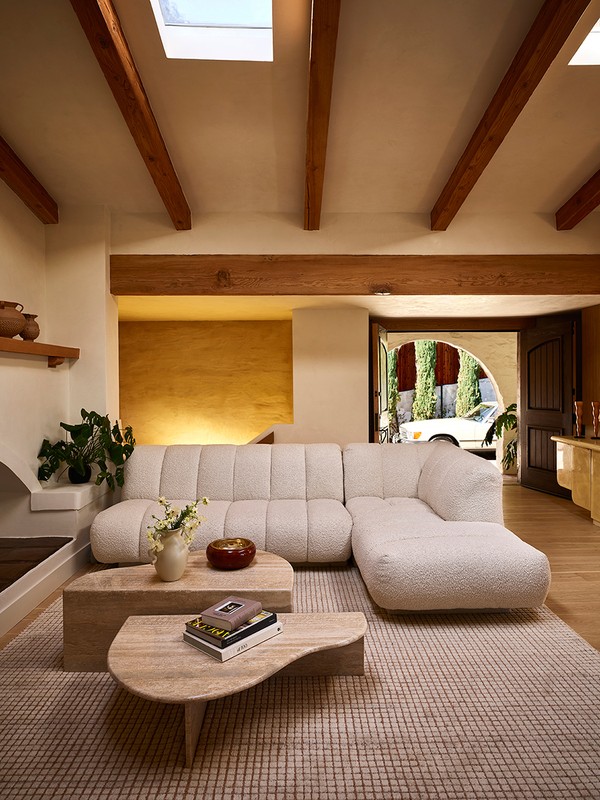 Living room interior with a cream-colored sectional sofa, stone coffee tables with books and flowers, and a neutral checkered rug.