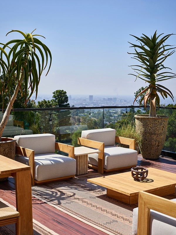 Outdoor patio featuring armchairs, a coffee table, and potted plants with a cityscape view on a sunny day.