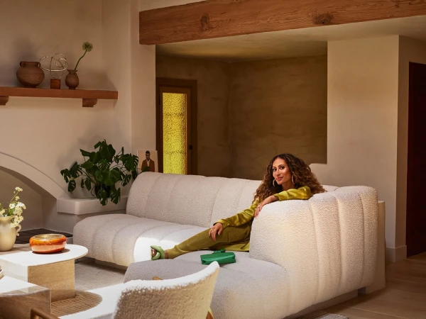 Woman with long curly hair seated on a white textured sectional sofa in a warm living room interior photographed by Frank Frances