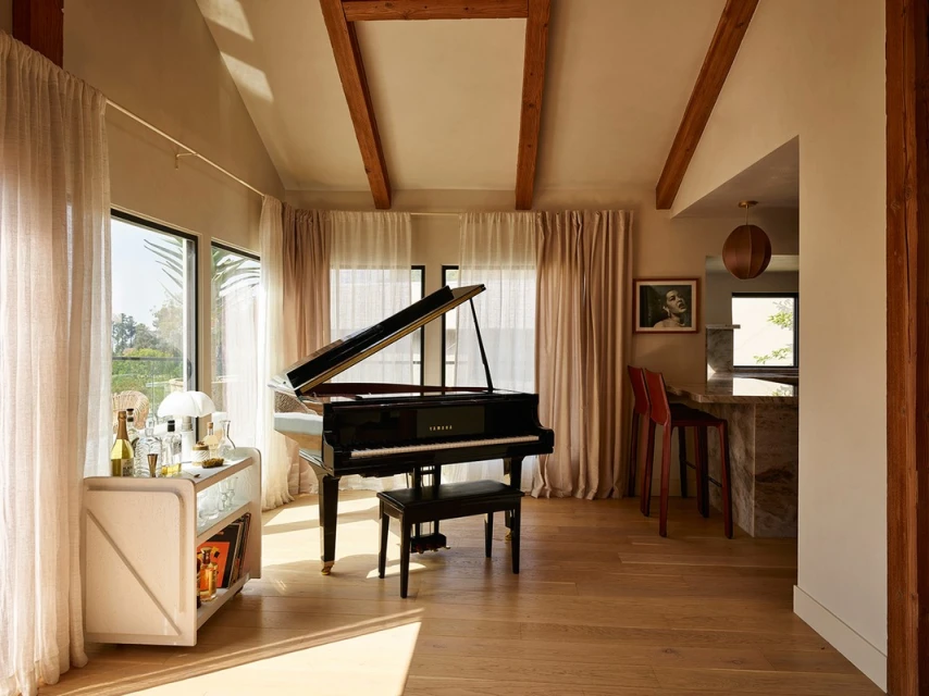 Interior view features a black grand piano with a bench, light wood flooring, and an open floor plan with a bar and natural light.