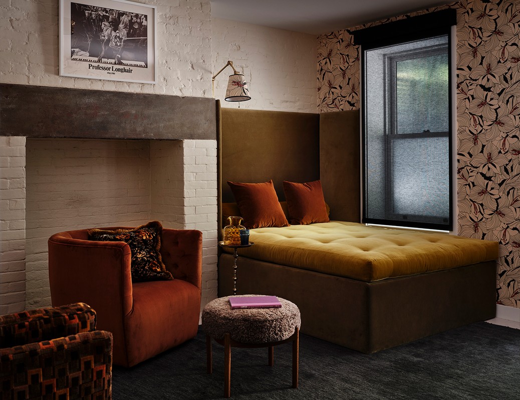 Cozy interior with orange armchair, footstool, olive daybed and textured wallpaper creates a warm, inviting atmosphere.