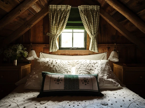 Cozy bedroom interior with a bed covered in embroidered white linens, patterned curtains, warm wood walls, and soft, diffused lighting.