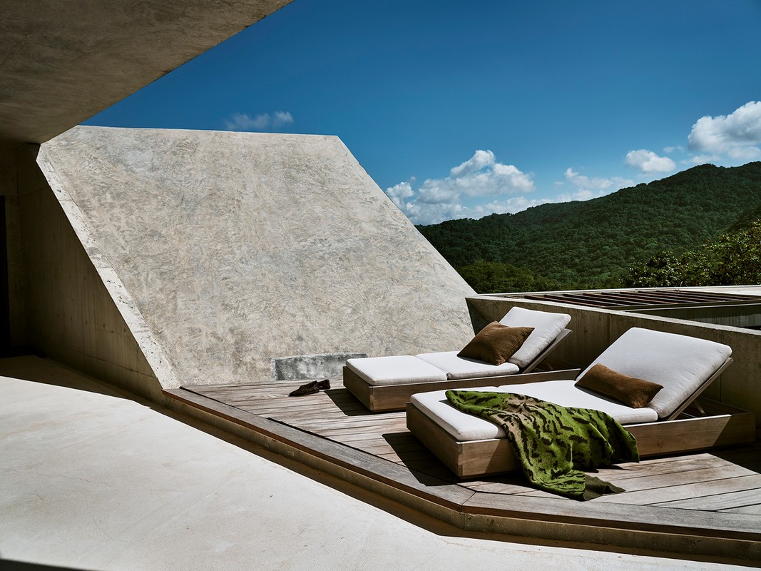 Outdoor terrace featuring two lounge chairs with cushions and throw pillows, set on a wooden deck with a mountain backdrop and blue sky.