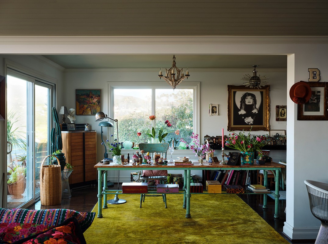 Eclectic home interior showcasing a green work desk with floral arrangements and books, bathed in natural light from a nearby window.