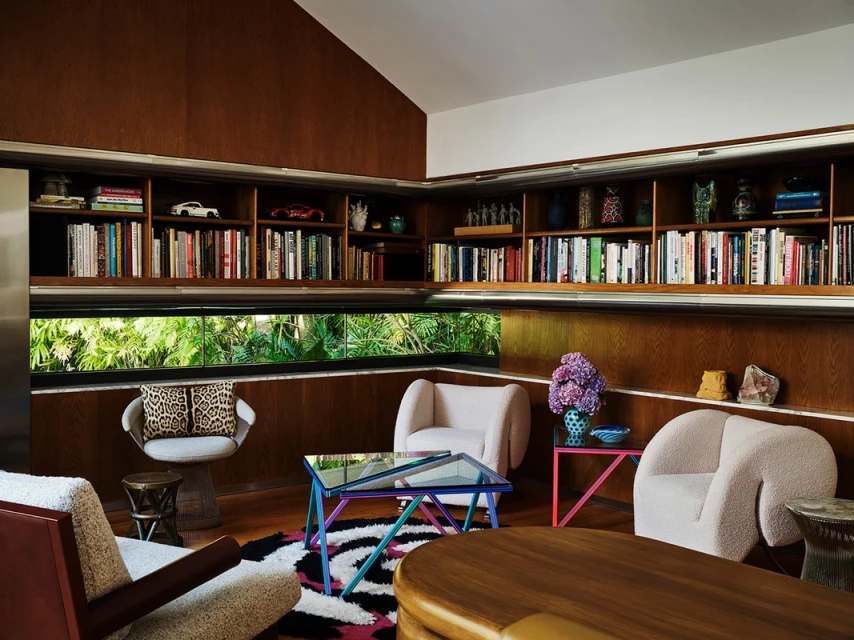 Stylish living room featuring bookshelves, a window with green foliage, and modern furniture arranged on a patterned rug.