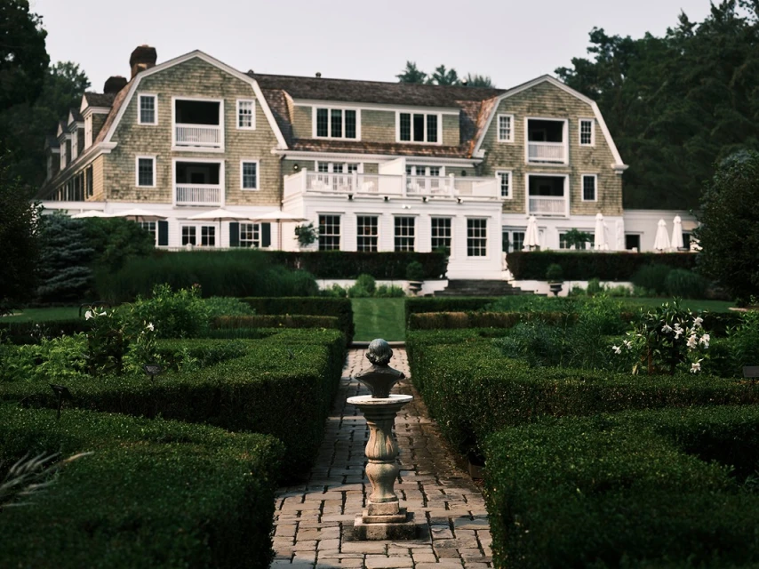 Exterior view of a large house with a manicured green garden and a stone path leading to the front, offering a tranquil residential setting.