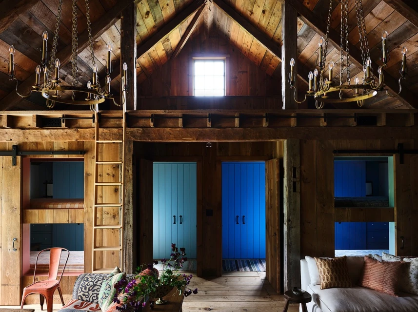 Rustic interior featuring wooden beams, vintage chandeliers, and a chair, creating a cozy and inviting space with a blend of natural and antique elements.