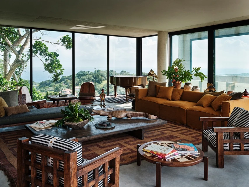 Living room interior showcasing a modern design with a large window offering a view of a lush green landscape and distant ocean.