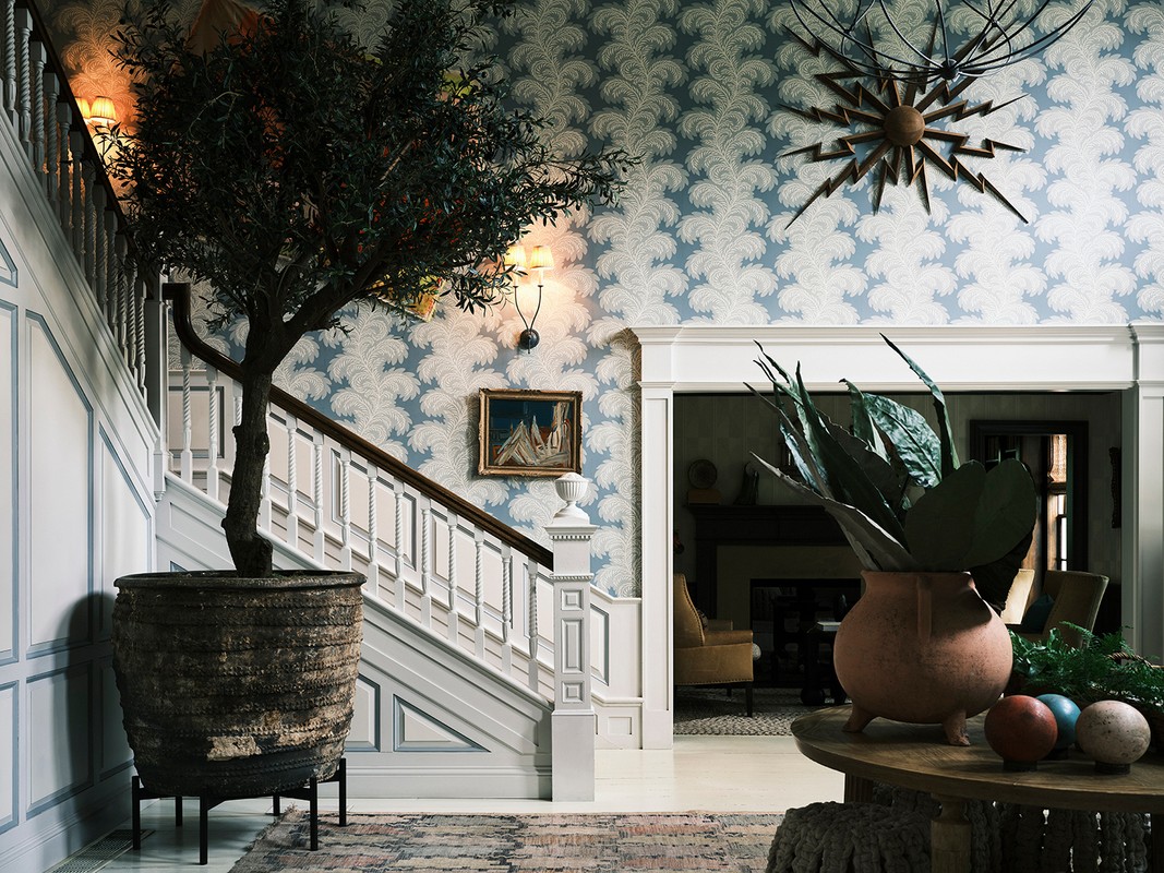 Ornate home interior with a large potted tree, decorative wallpaper, a staircase, and interior design elements.