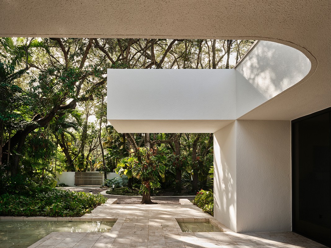 Outdoor view of modern building exterior with white concrete walls, water feature, and lush trees under natural light. Architecture design.