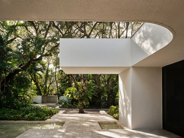 Outdoor view of modern building exterior with white concrete walls, water feature, and lush trees under natural light. Architecture design.