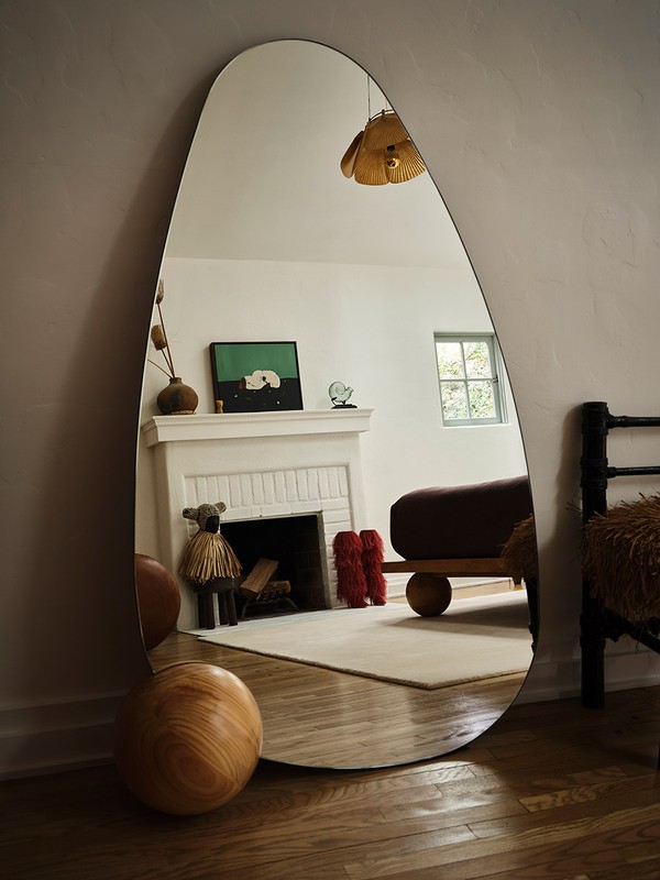 Modern interior design: A full-length mirror reflects a minimalist living room with a fireplace, artwork, and wood flooring.