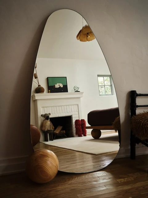 Modern interior design: A full-length mirror reflects a minimalist living room with a fireplace, artwork, and wood flooring.