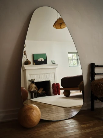 Modern interior design: A full-length mirror reflects a minimalist living room with a fireplace, artwork, and wood flooring.