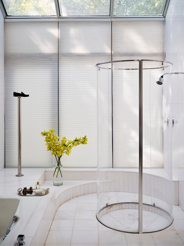 Bright, modern bathroom featuring a clear glass shower, tiled floors and walls, yellow flowers, and a window with blinds.