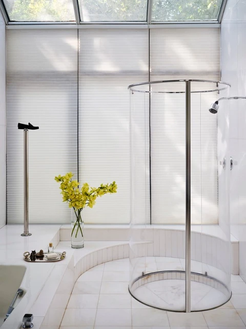 Bright, modern bathroom featuring a clear glass shower, tiled floors and walls, yellow flowers, and a window with blinds.