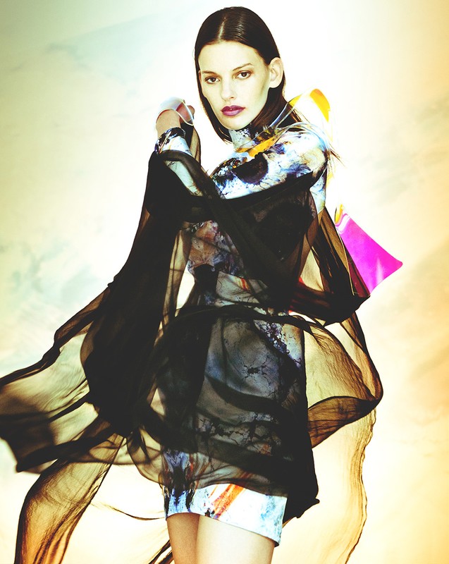 A fashion shot features a slim adult woman in a flowy black dress against a soft, diffused background, blending fashion and art.