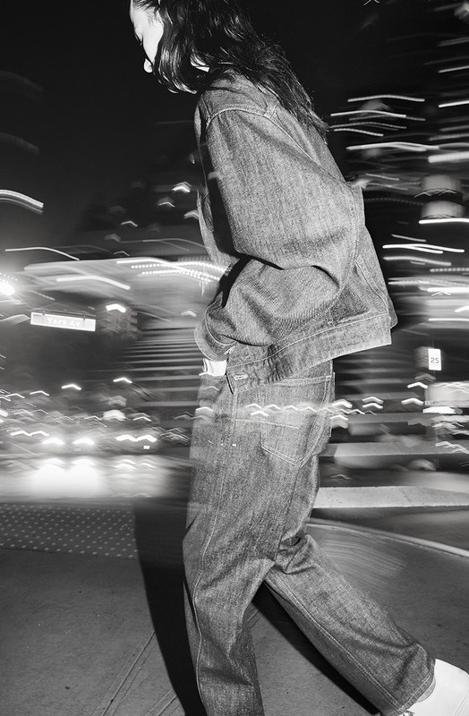 Model in denim jacket and jeans walking through a city street with motion blur effects in black and white