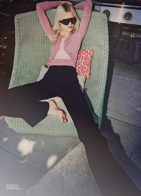 Woman in sunglasses reclines in a wicker chair on a patio, wearing a pink top and dark pants, with a grill visible in the background.